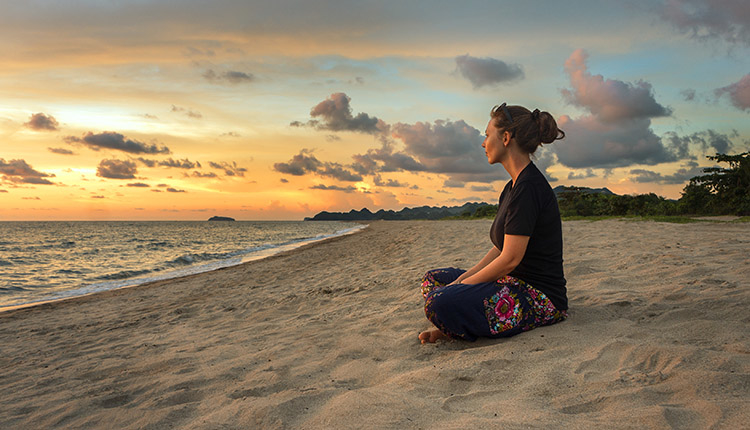 Woman sitting on a beach at sunset. Press pause to advance your security career..